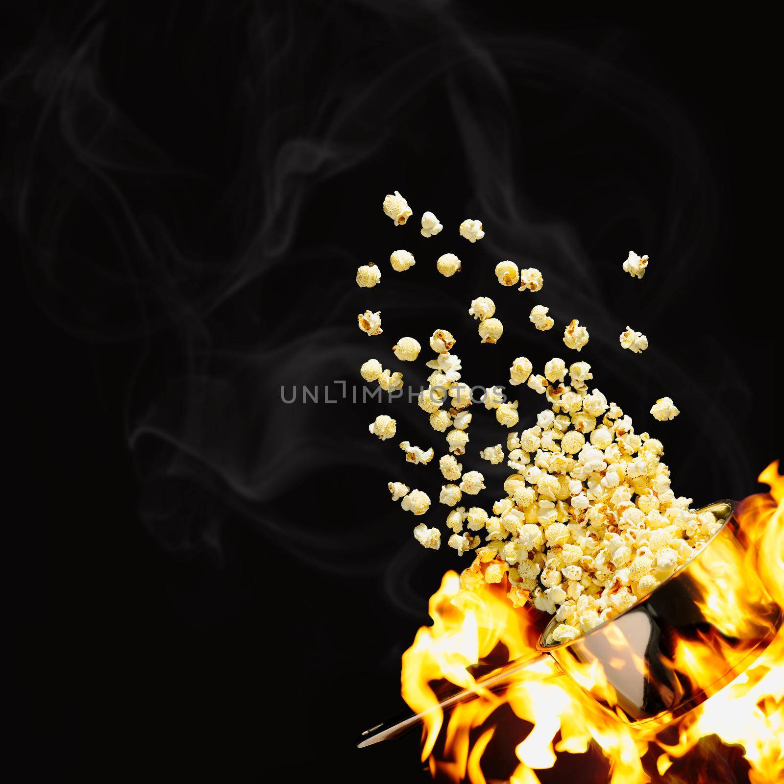 Flying popcorn on a dark background. Hot popcorn flying from pot under fire. Advertising concept. by PhotoTime