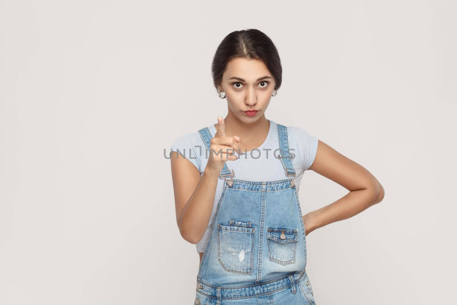 Warning sign. Young adult middle eastern woman, looking at camera with serious face and finger warning. Studio shot. Gray background.