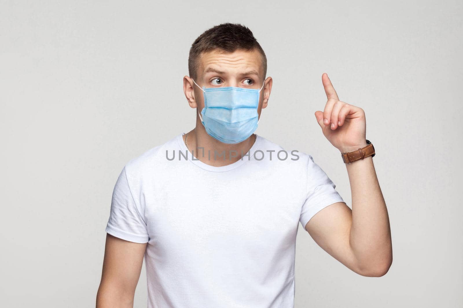 I have idea. Portrait of thoughtful young man in white shirt with surgical medical mask standing and try to remember his idea. indoor studio shot, isolated on gray background.