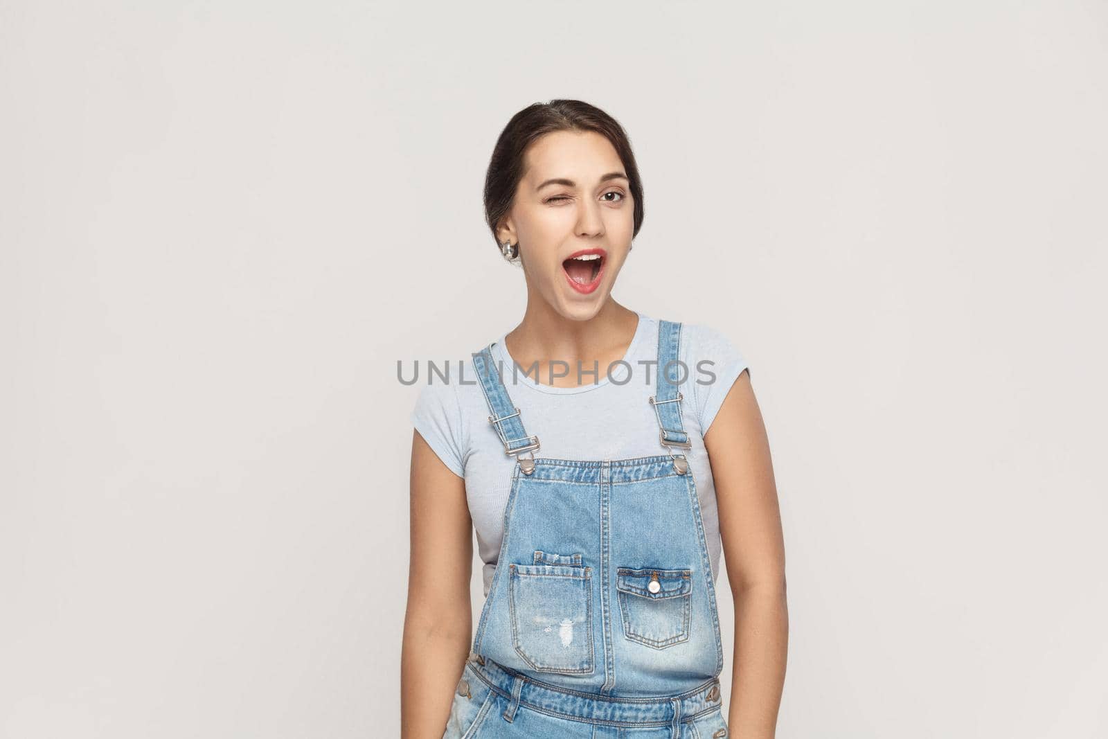 The young adult beautiful arab woman, toothy smile and wink at camera. Isolated studio shot on gray background