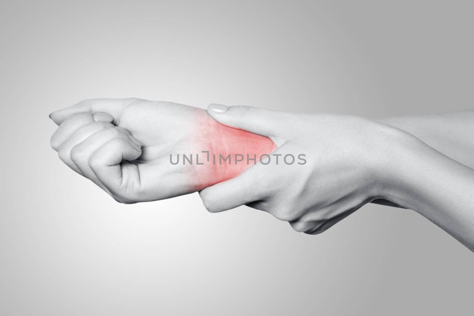 Closeup view of a young woman with pain on hand on gray background. Black and white photo with red dot.