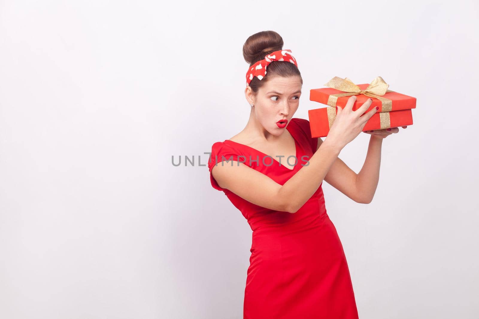 Cunning woman, looking inside gift box . Indoor, studio shot, isolated on gray background