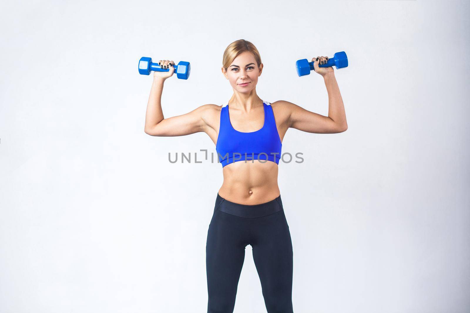 Blonde woman with perfect body, holding two blue dumbbells. Studio shot