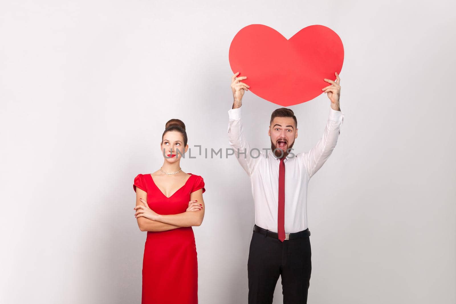 Woman in red dress thinking, happiness man holding red heart. Indoor, studio shot, isolated on gray background