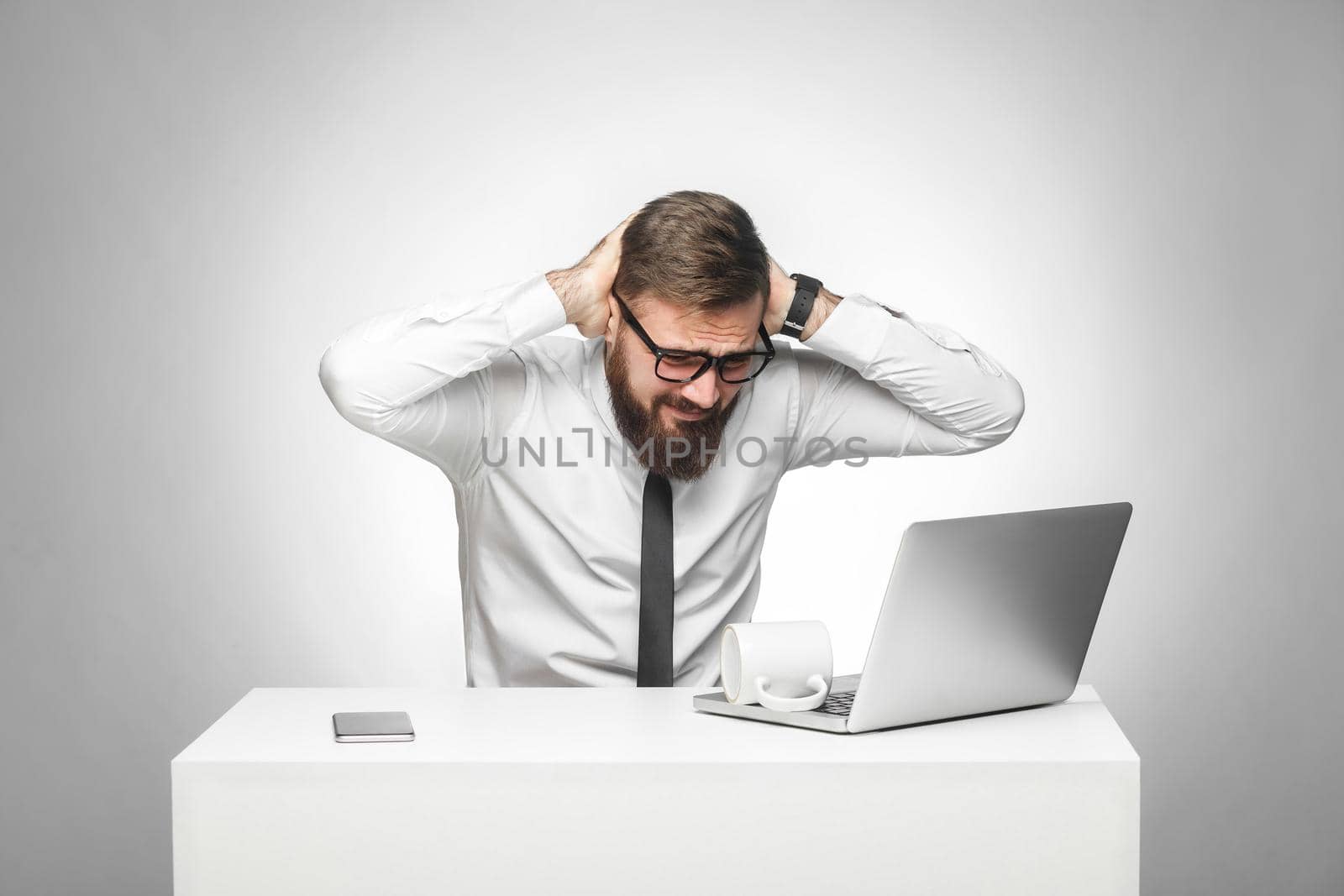 No way! Portrait of unhealphy painful young manager in white shirt and black tie are sitting in office and have strong headache, holding hands on head. Studio shot, isolated, gray background, indoor