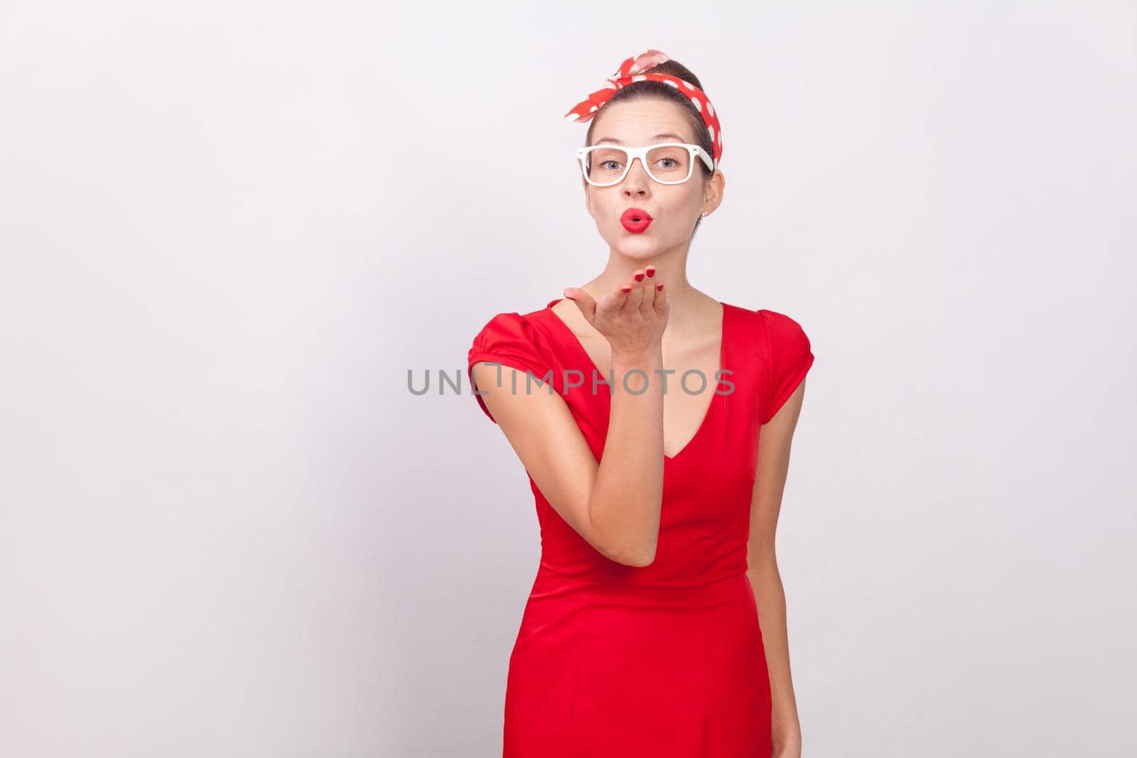 Cute beautiful woman send air kiss with love. Indoor, studio shot, isolated on gray background