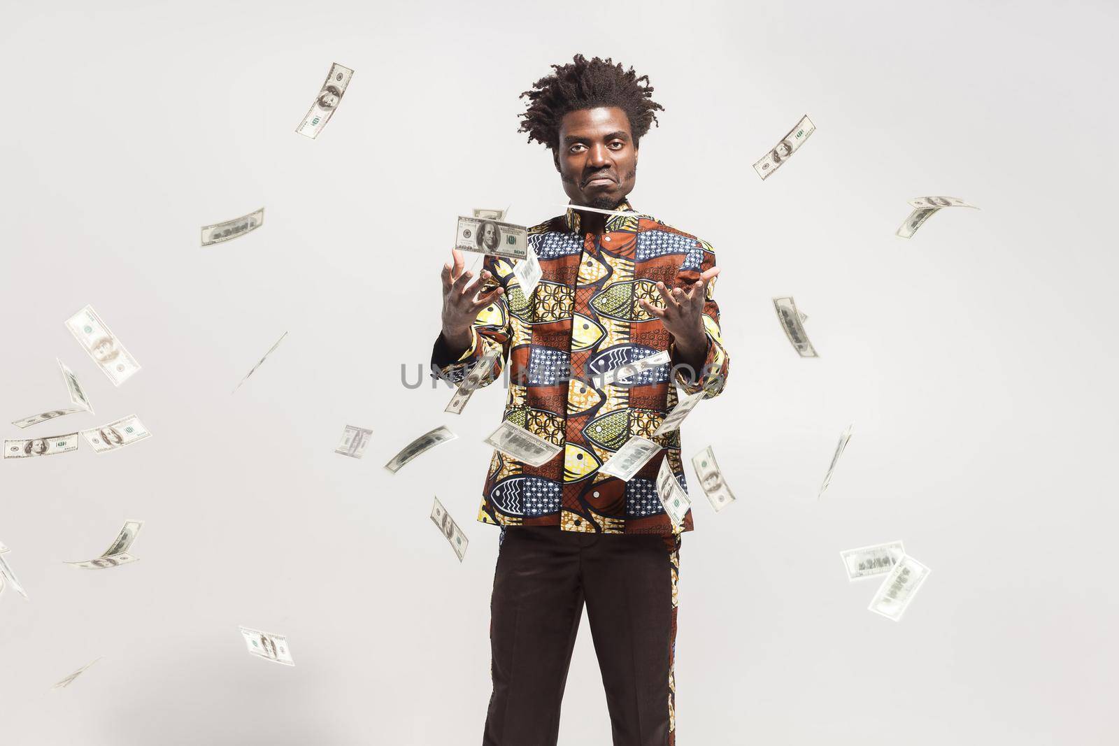 Many cash fly near african man in national kongo costume. Indoor, isolated on gray background