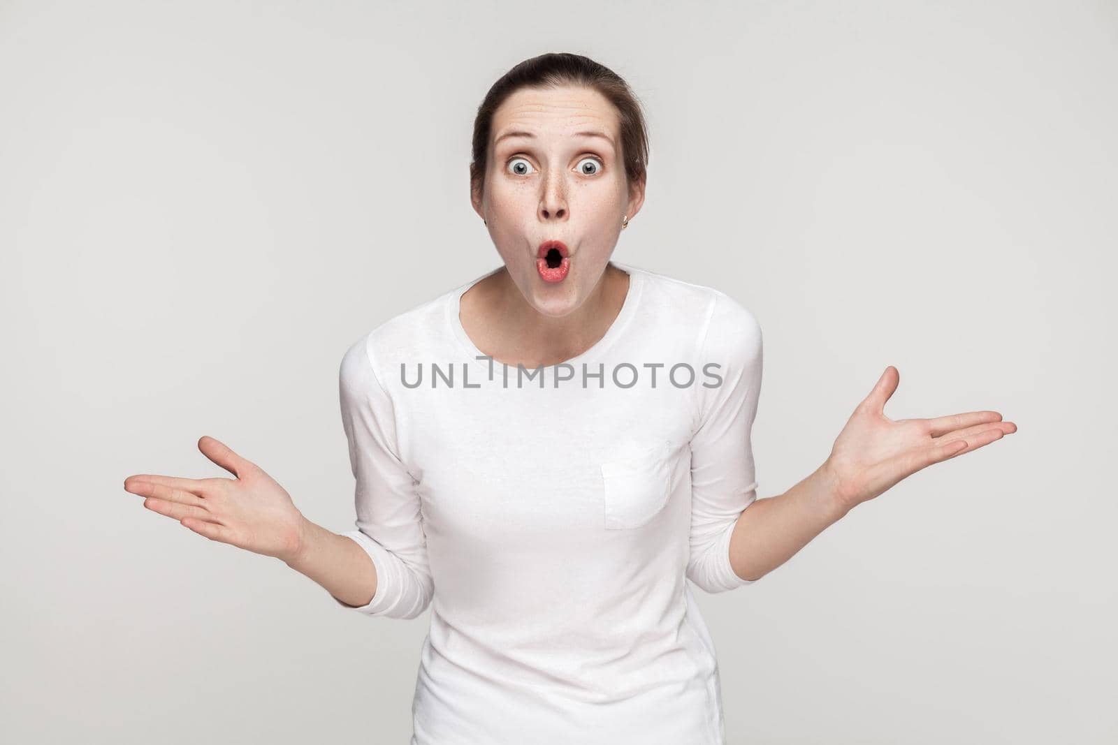 Surprised young woman looking at camera with open mouth and big eyes. Studio shot, gray background