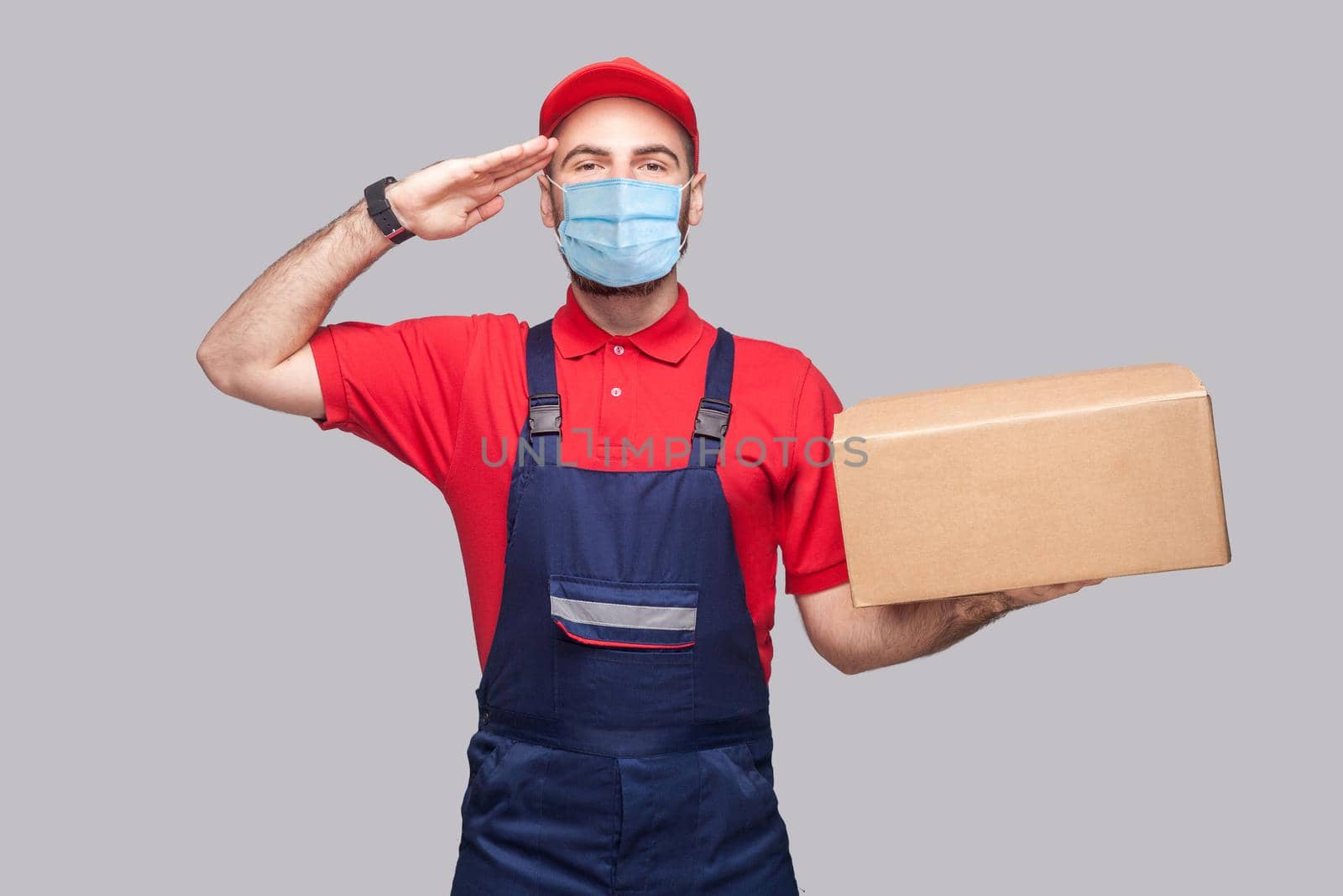 man in overall standing, holding cardboard box on grey background. by Khosro1