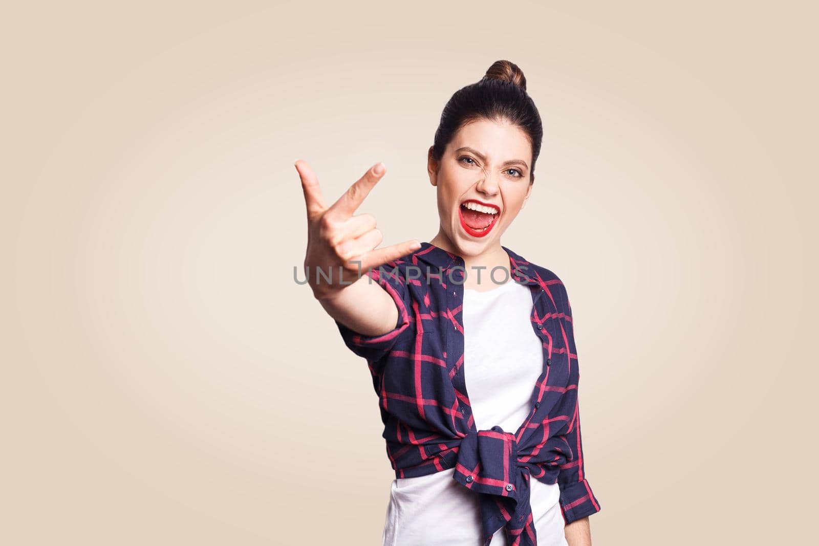 Rock sign. Happy funny toothy smiley young woman showing Rock sign with fingers. studio shot on beige background. focus on face.