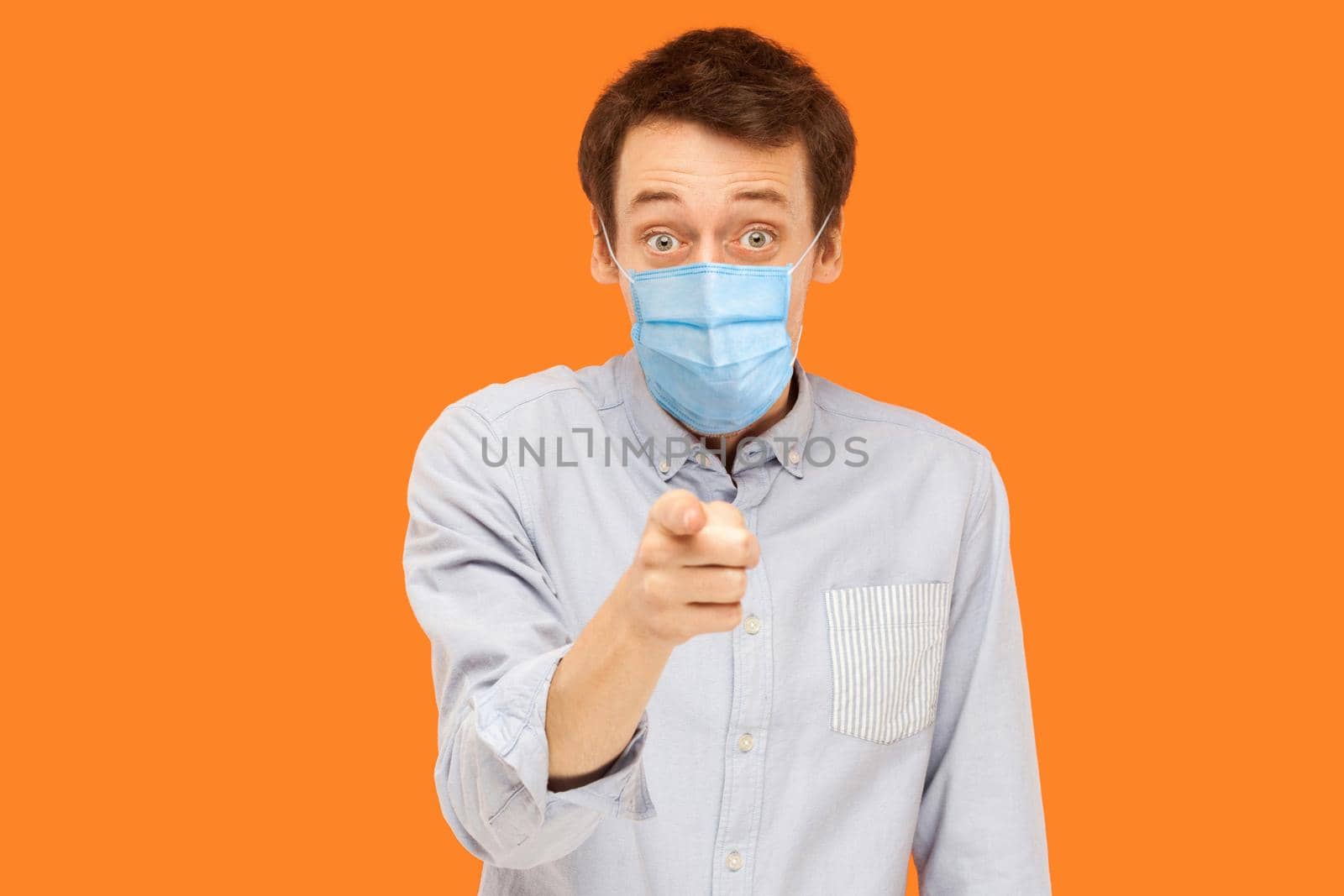 You? Portrait of shocked or surprised young worker man with surgical medical mask standing pointing and looking at camera with amazed face and asking. indoor studio shot isolated on orange background.