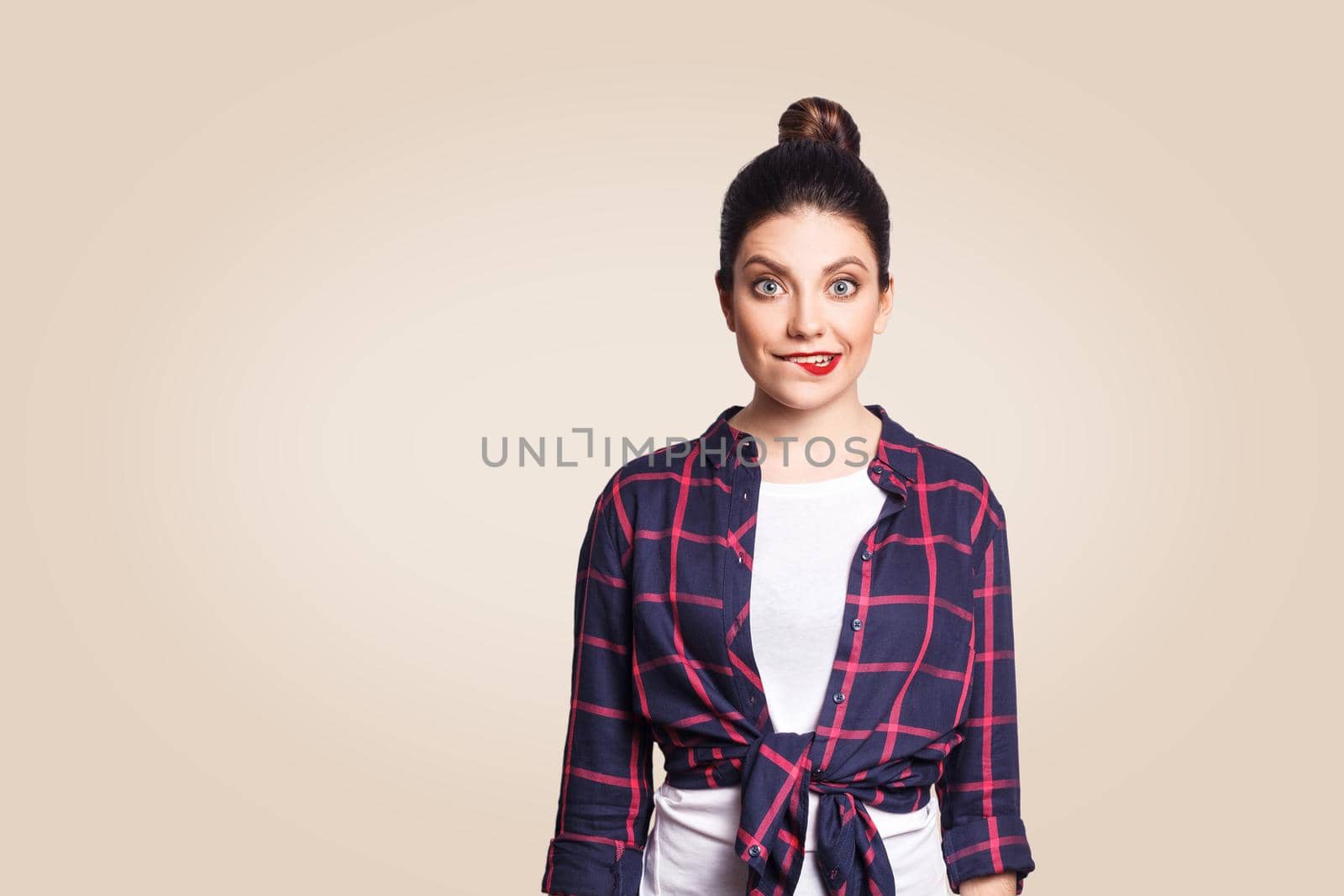 Portrait of beautiful happy funny girl in casual style looking at camera with big eyes and biting lips. studio shot on beige background.