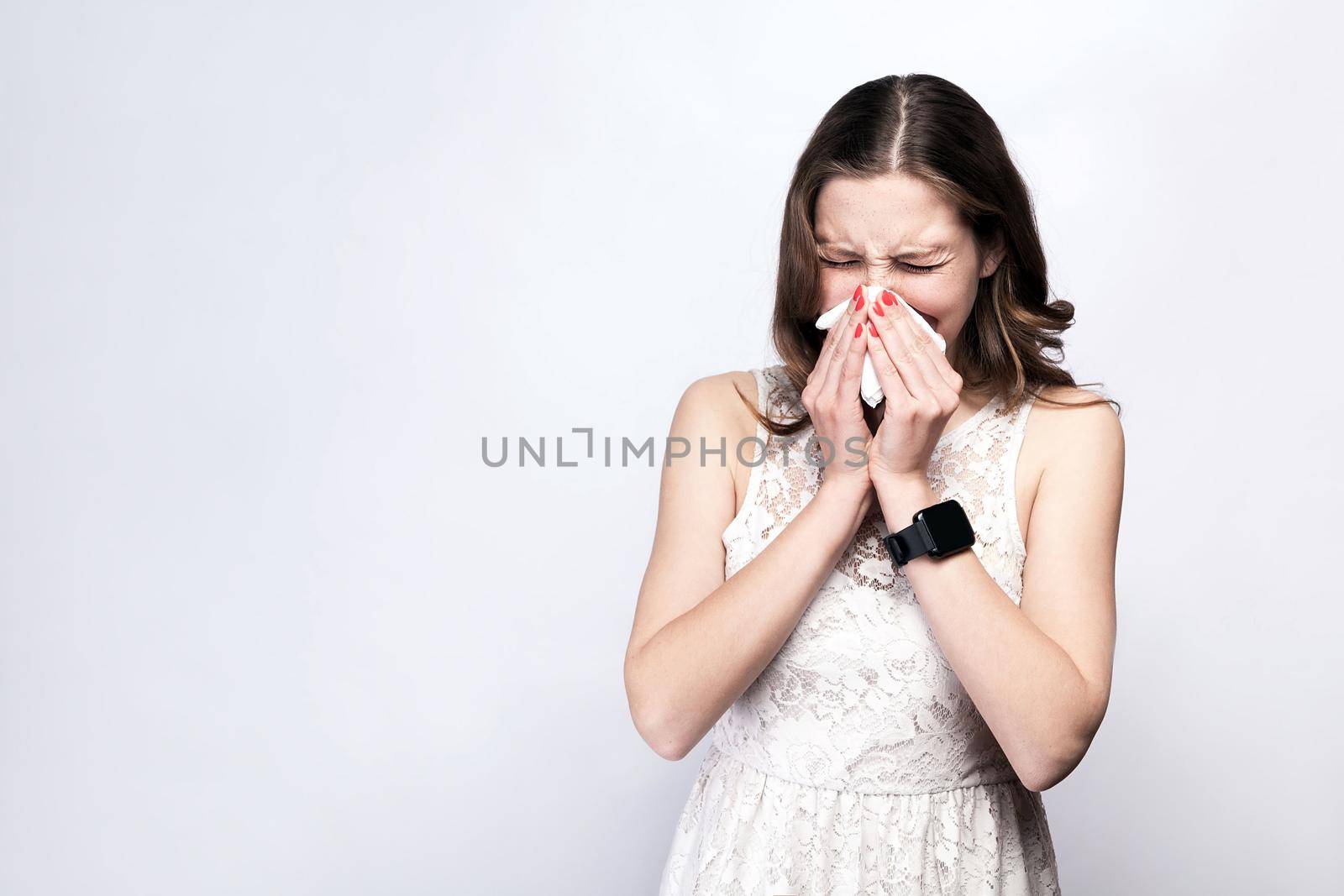 Portrait of sick cold woman with freckles and white dress and smart watch on silver gray background. healthcare and medicine concept.