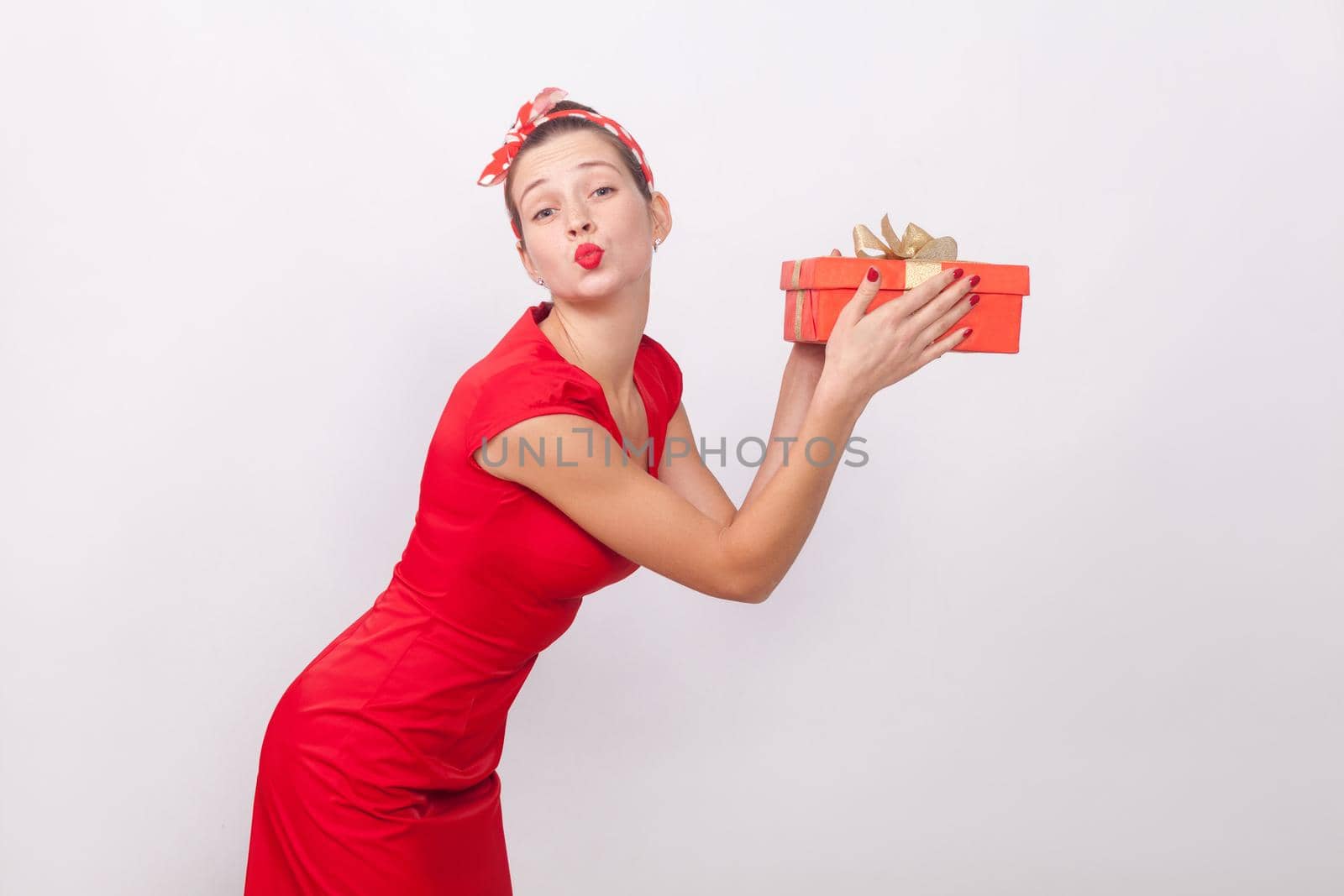 Beautiful and happy woman holding gift box, send air kiss. Indoor, studio shot, isolated on gray background