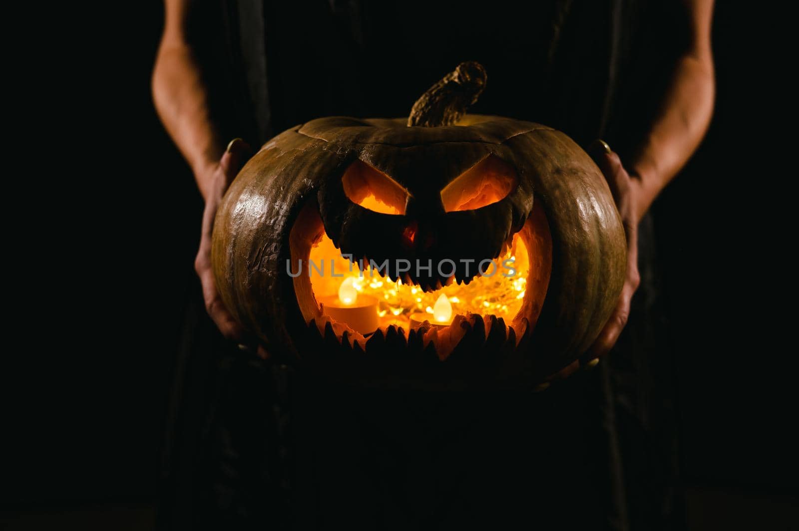 The witch is holding a pumpkin jack o lantern glowing in the dark. Halloween