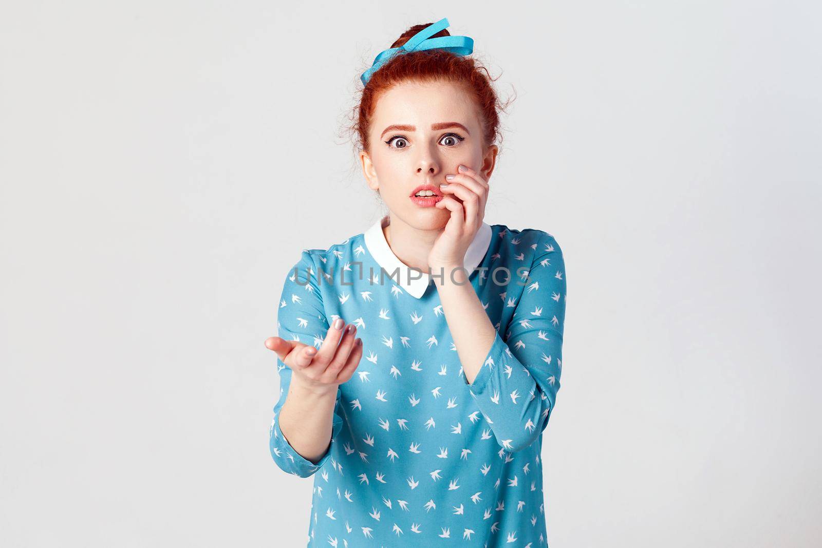 Human facial expressions, emotions and feelings. Beautiful redhead girl with hair knot having scared and frightened look, keeping mouth open, touching face and pointing hand at camera.