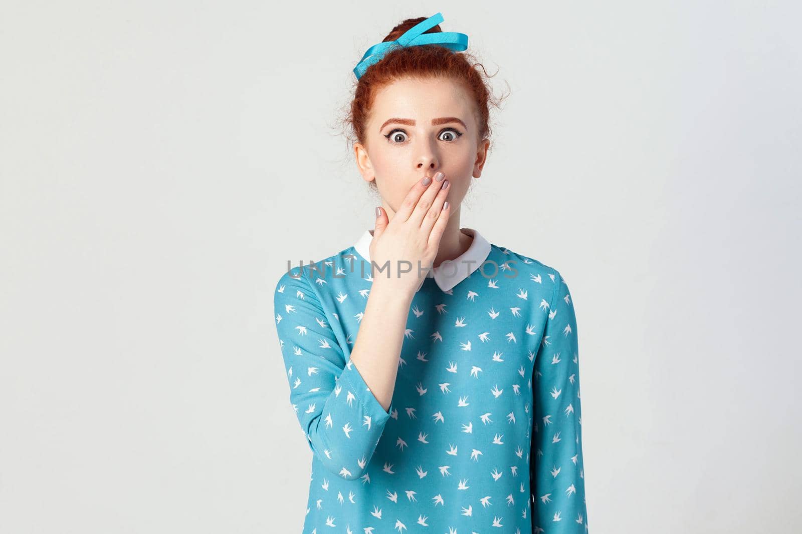 Human face expressions and emotions. Female in despair and shock. The young redhead girl in shoked, looking panic, covered her mouth by hand. Isolated studio shot on gray background.