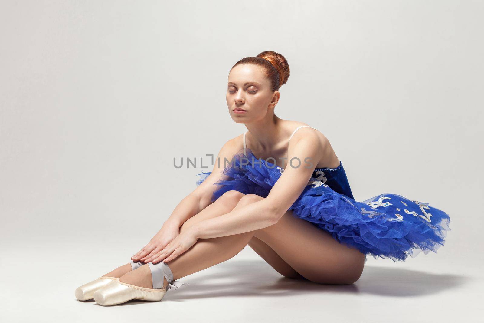 ballerina with closed eyes in blue dress and pointe shoes sitting on white floor. by Khosro1