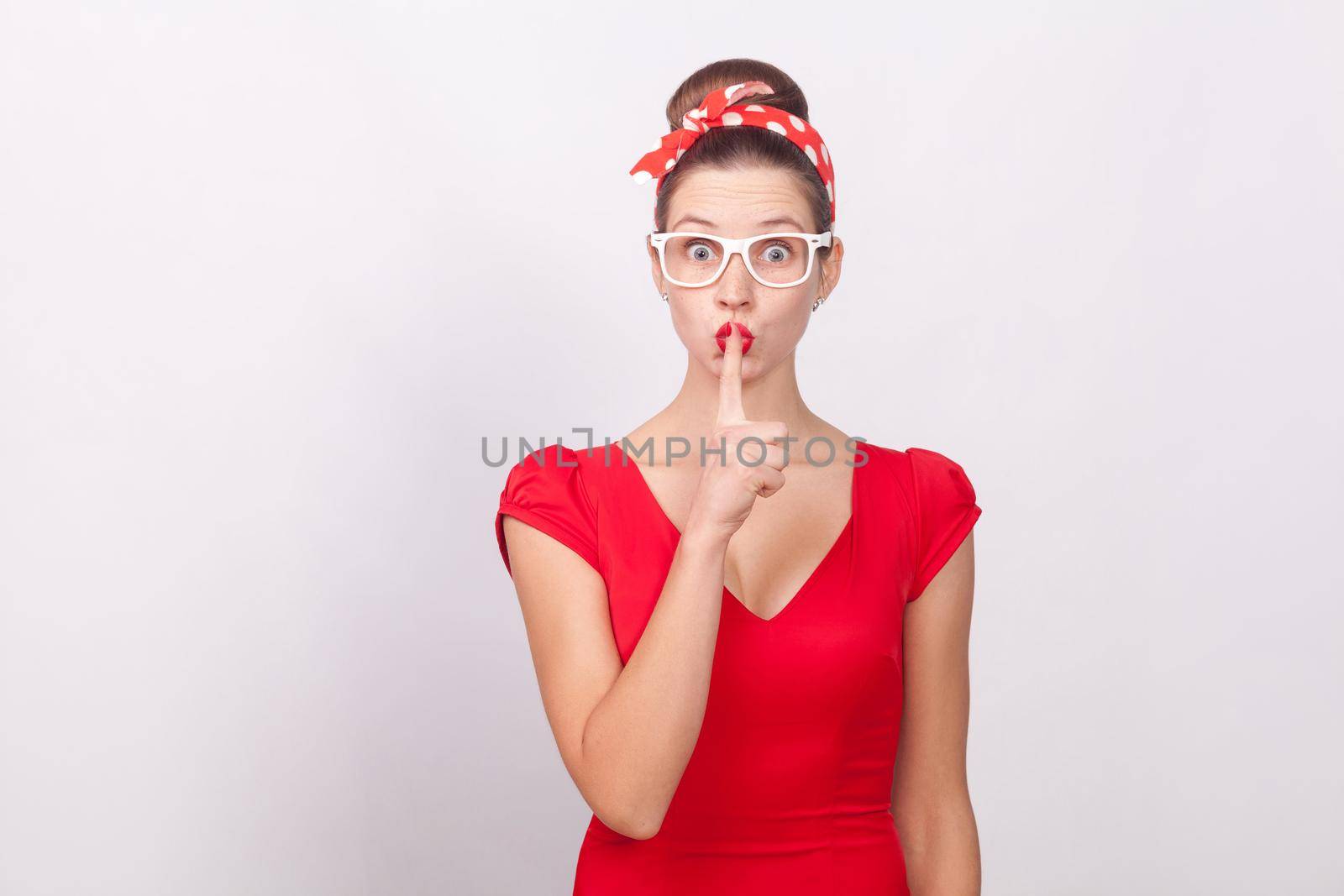 Woman in red dress and dots bandsge, showing secret sign. Indoor, studio shot, isolated on gray background