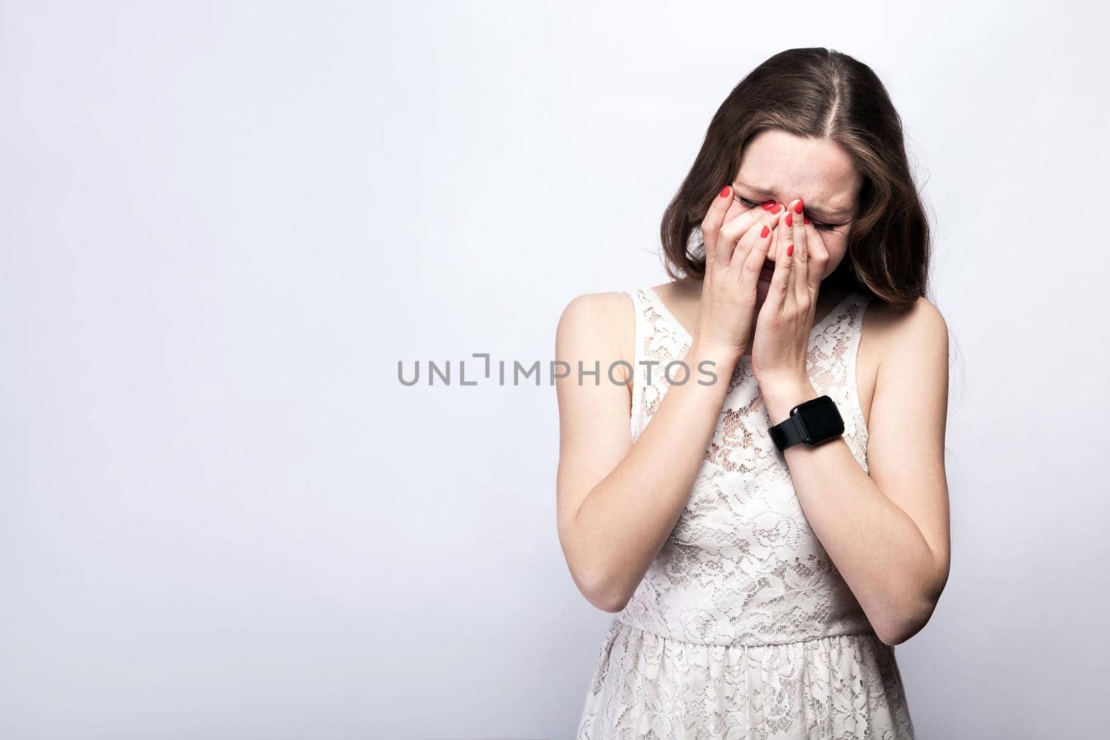 sad, unhappy crying woman with freckles and white dress and smart watch on silver gray background by Khosro1