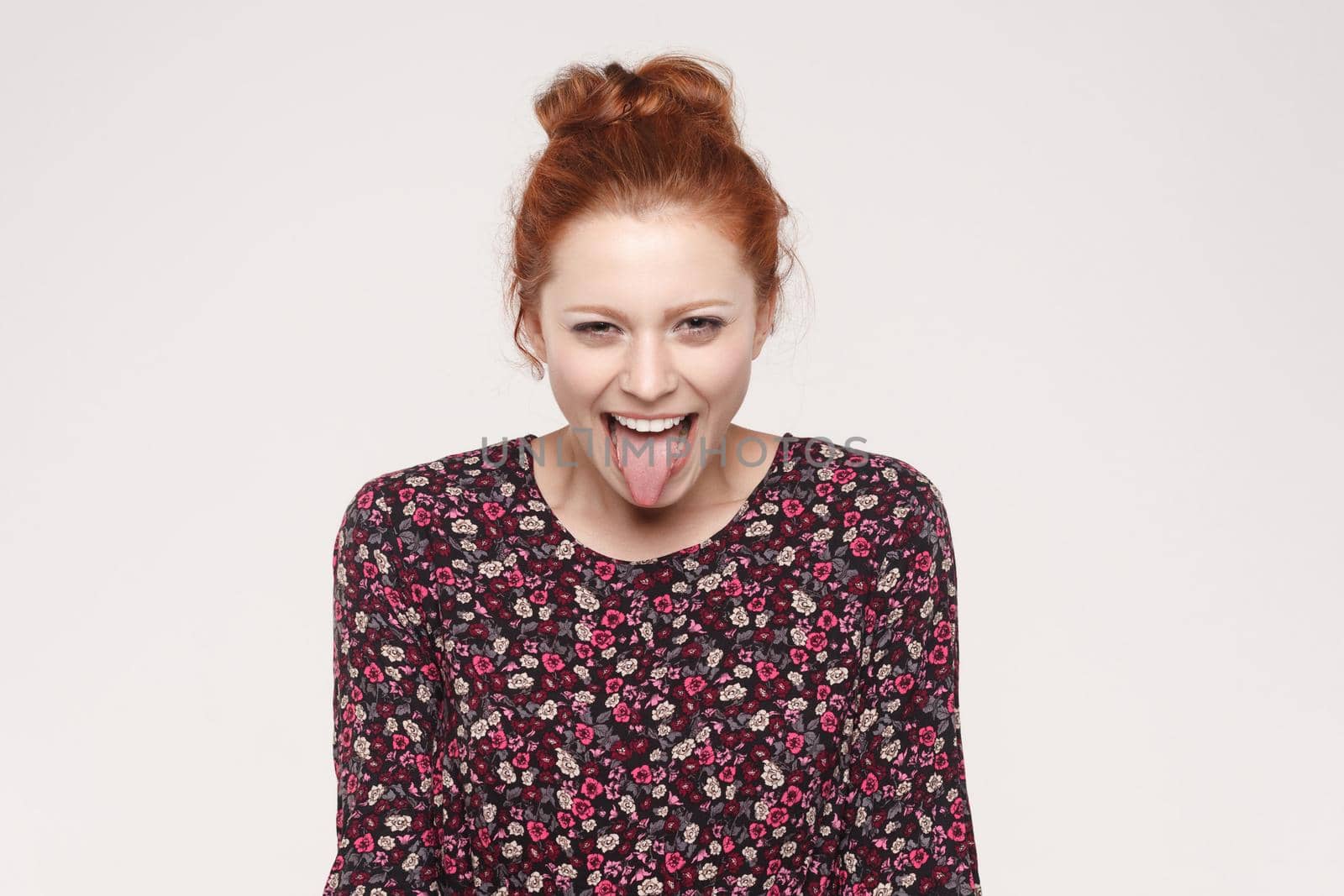 Happiness ginger woman looking at camera and tongue out. Indoor on gray background, studio shot