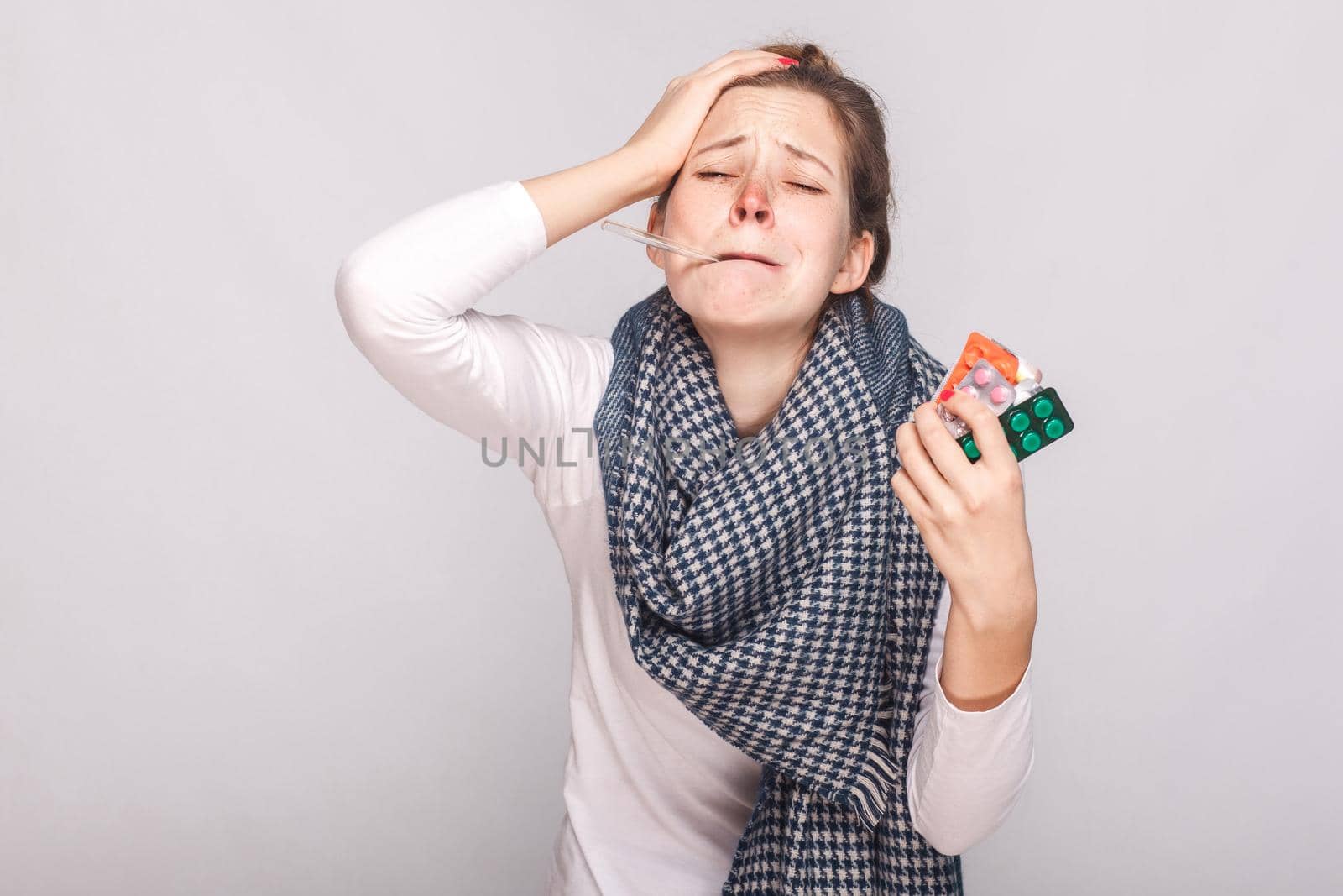 Young adult sick woman have temperature, holding many pills. Studio shot, isolated on gray background