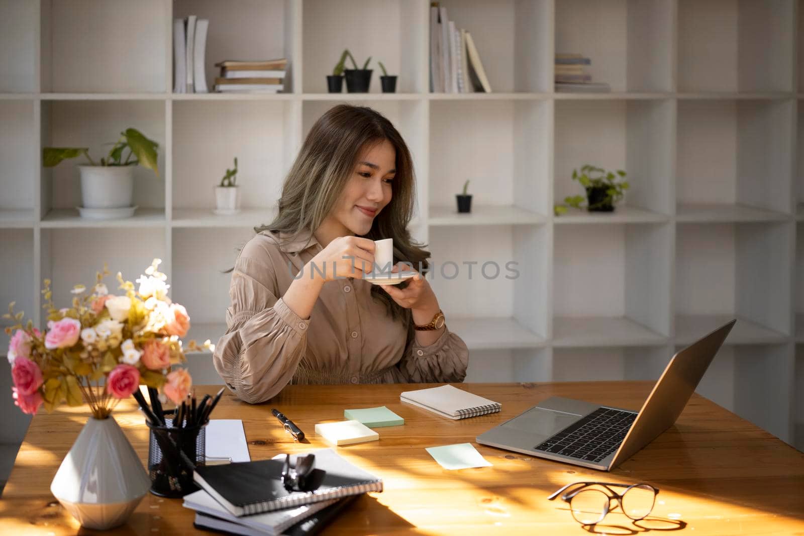 Pleased beautiful business woman reading news on laptop computer and drinking hot coffee.