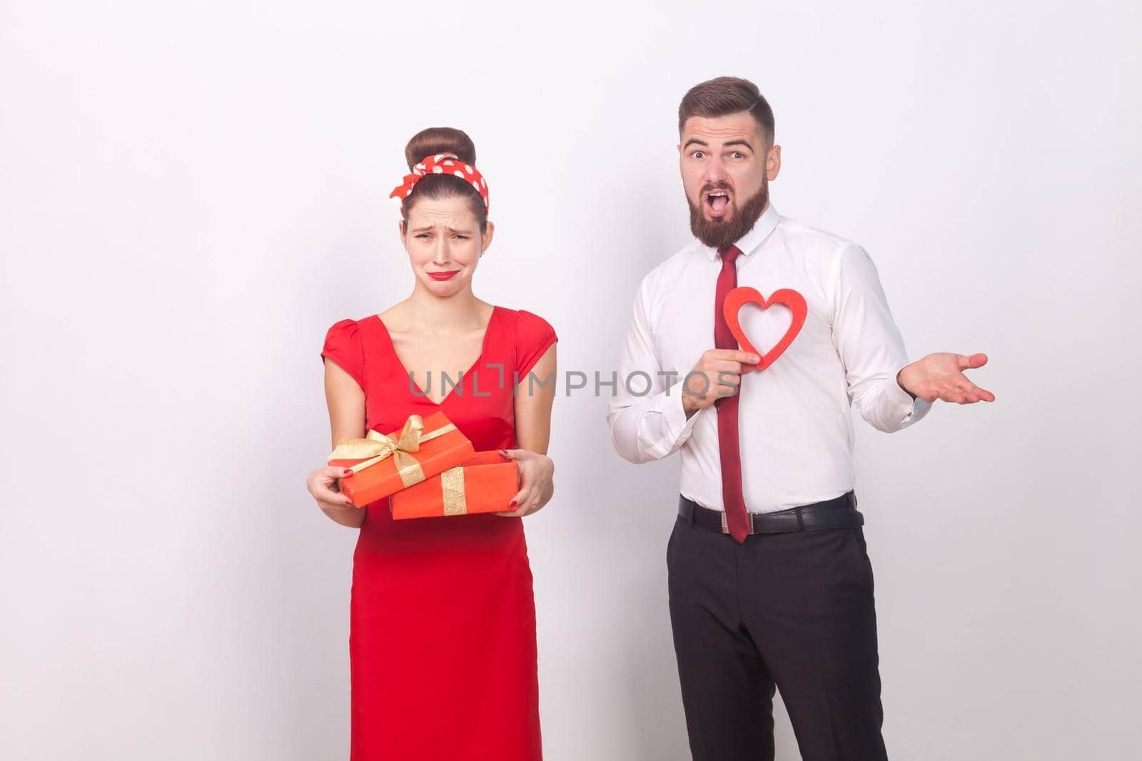 Disappointment. Woman holding gift box and cry, man confused. Indoor, studio shot, isolated on gray background