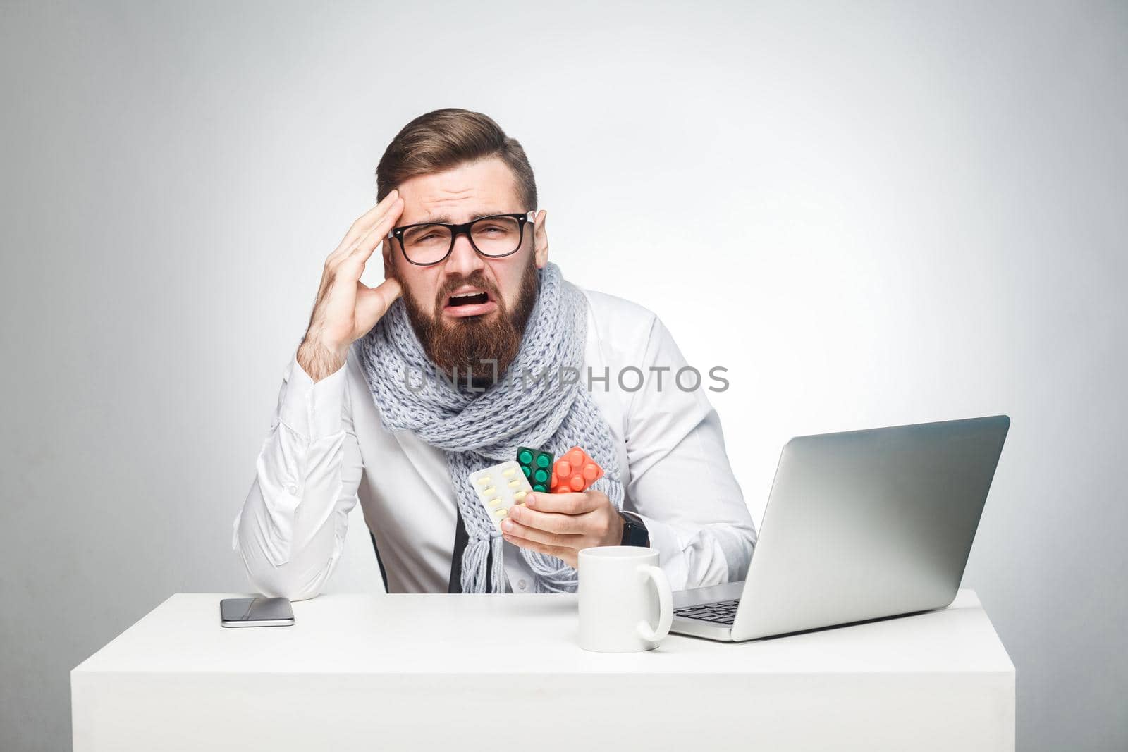 Portrait of unhealthy tired young man in white shirt, scarf and black tie are sitting in office and need to finish important report, have grippe virus. Studio shot, isolated, gray background, indoor