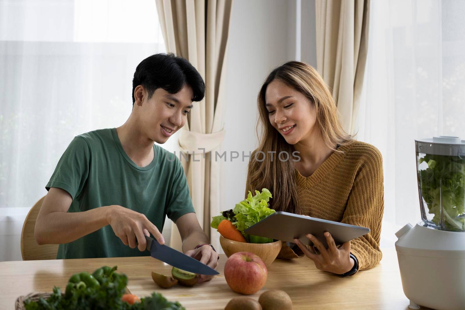 Young couple searching menu on digital tablet and preparing vegetarian lunch in kitchen. by prathanchorruangsak