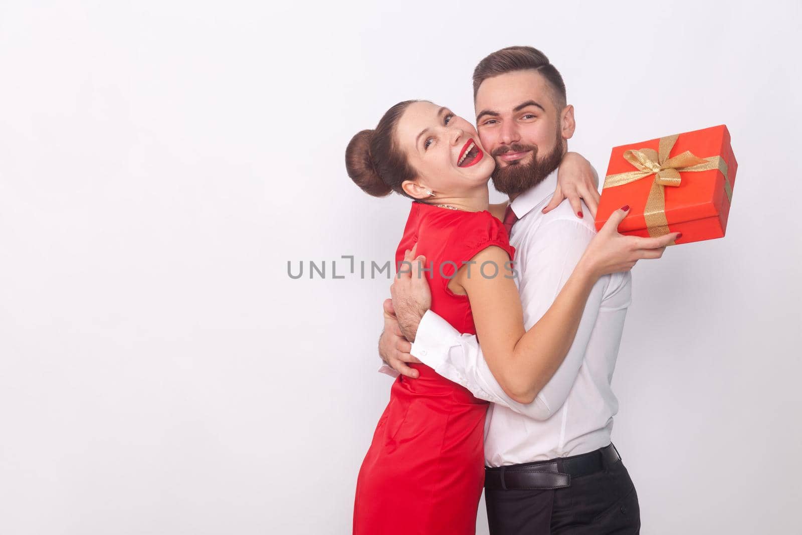 It's present for you! Couple hugging, woman holding gift box. Indoor, studio shot, isolated on gray background