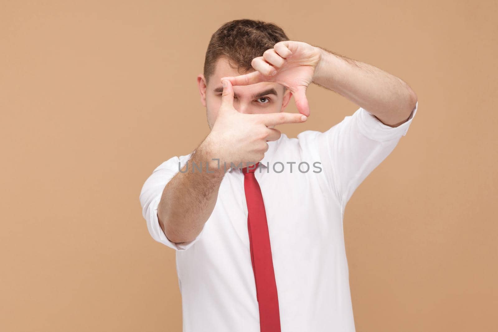 Man showing frame photographer sign at camera. Business people concept, good and bad emotion and feelings. Studio shot, isolated on light brown background