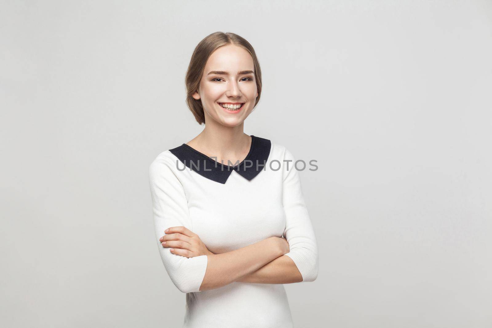 Businesswoman crossed hands, toothy smiling and looking at camera. Studio shot, gray background