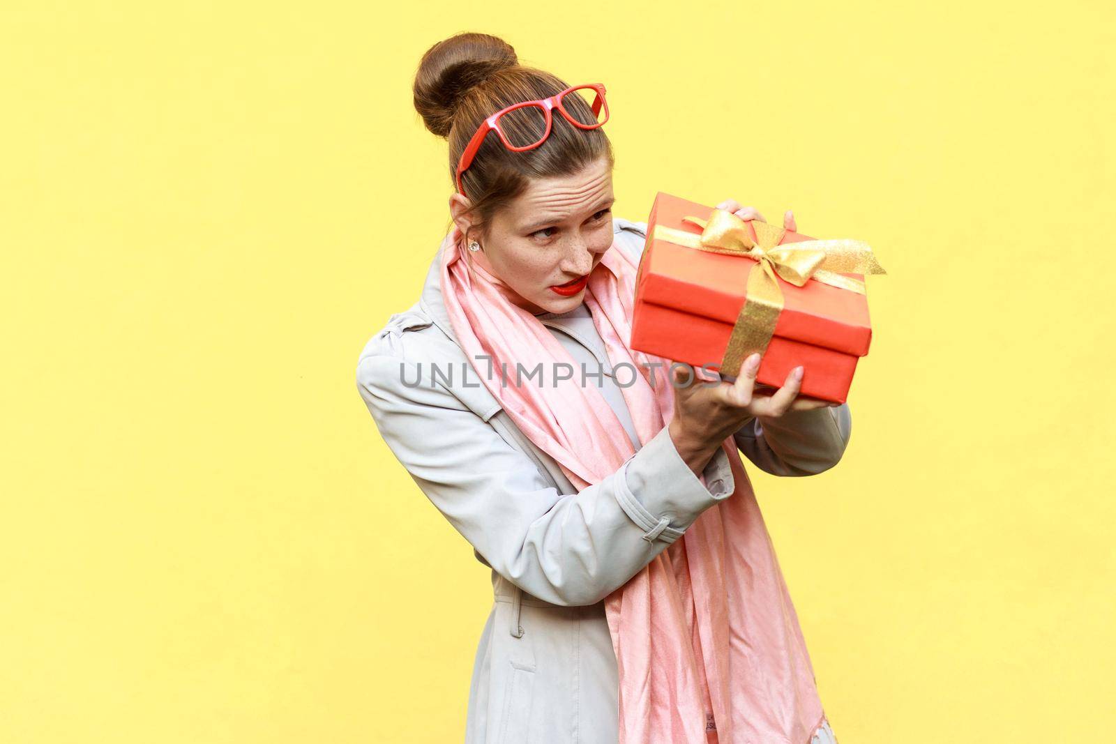 Hmm what is it! Cunning woman looking at gift box and want too open. Yellow background. Studio shot