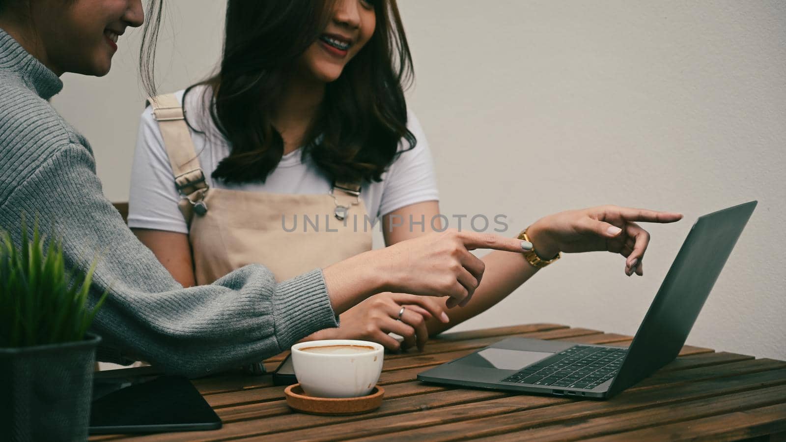 Cropped shot two smiling young asian women pointing on screen of computer laptop. by prathanchorruangsak