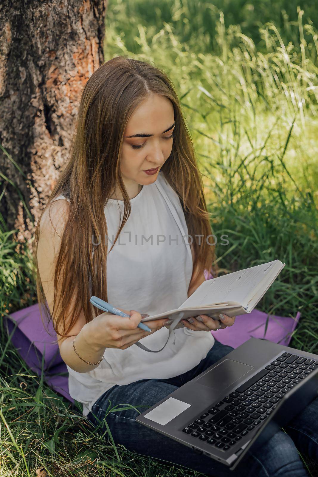 the girl sits on the grass and uses a laptop. Education, lifestyle, technology concept, outdoor learning concept by Anyatachka