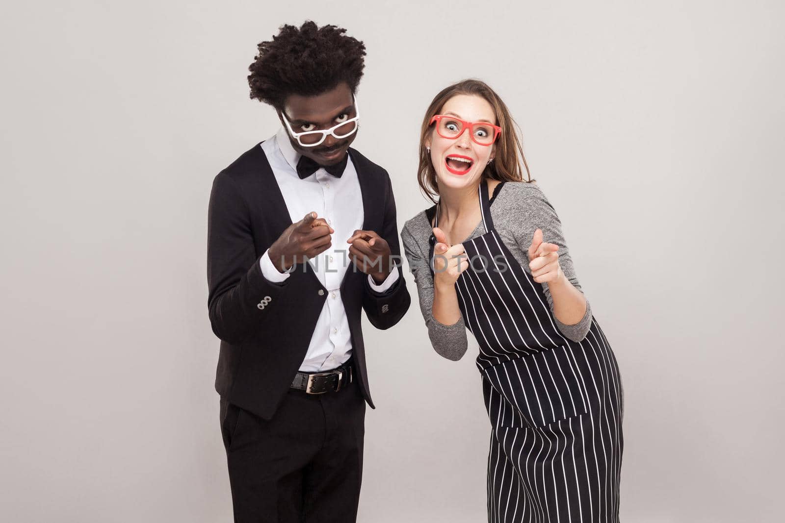 Mixed race couple pointing fingers at camera and smiling. Studio shot, gray background