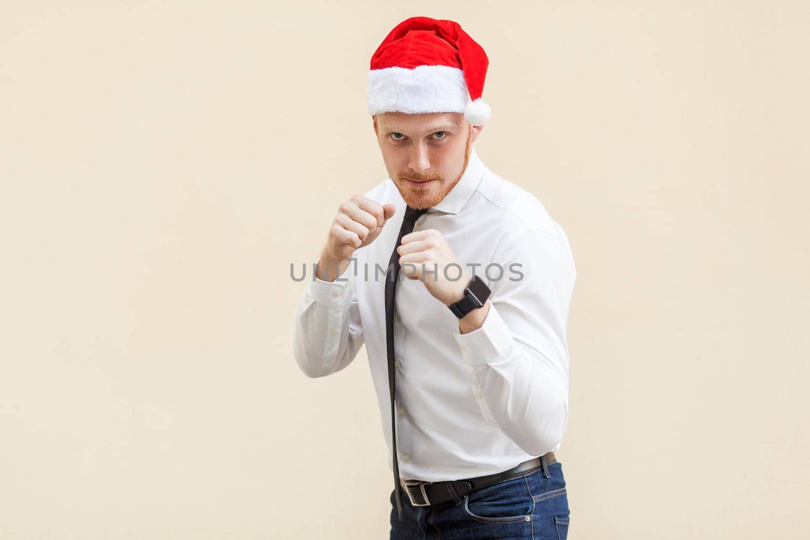 Boxing. Young adult ginger businessman on red santa hat, ready for fight on light orange background. by Khosro1