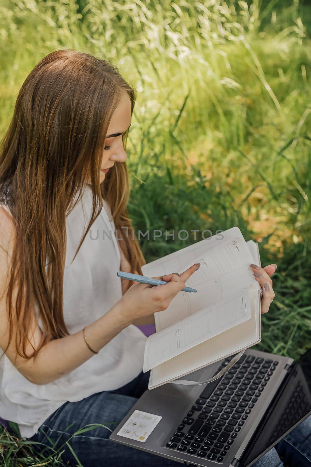 On the banner, a young girl works with a laptop in the fresh air in the park, sitting on the lawn. The concept of remote work. Work as a freelancer. The girl takes courses on a laptop and smiles