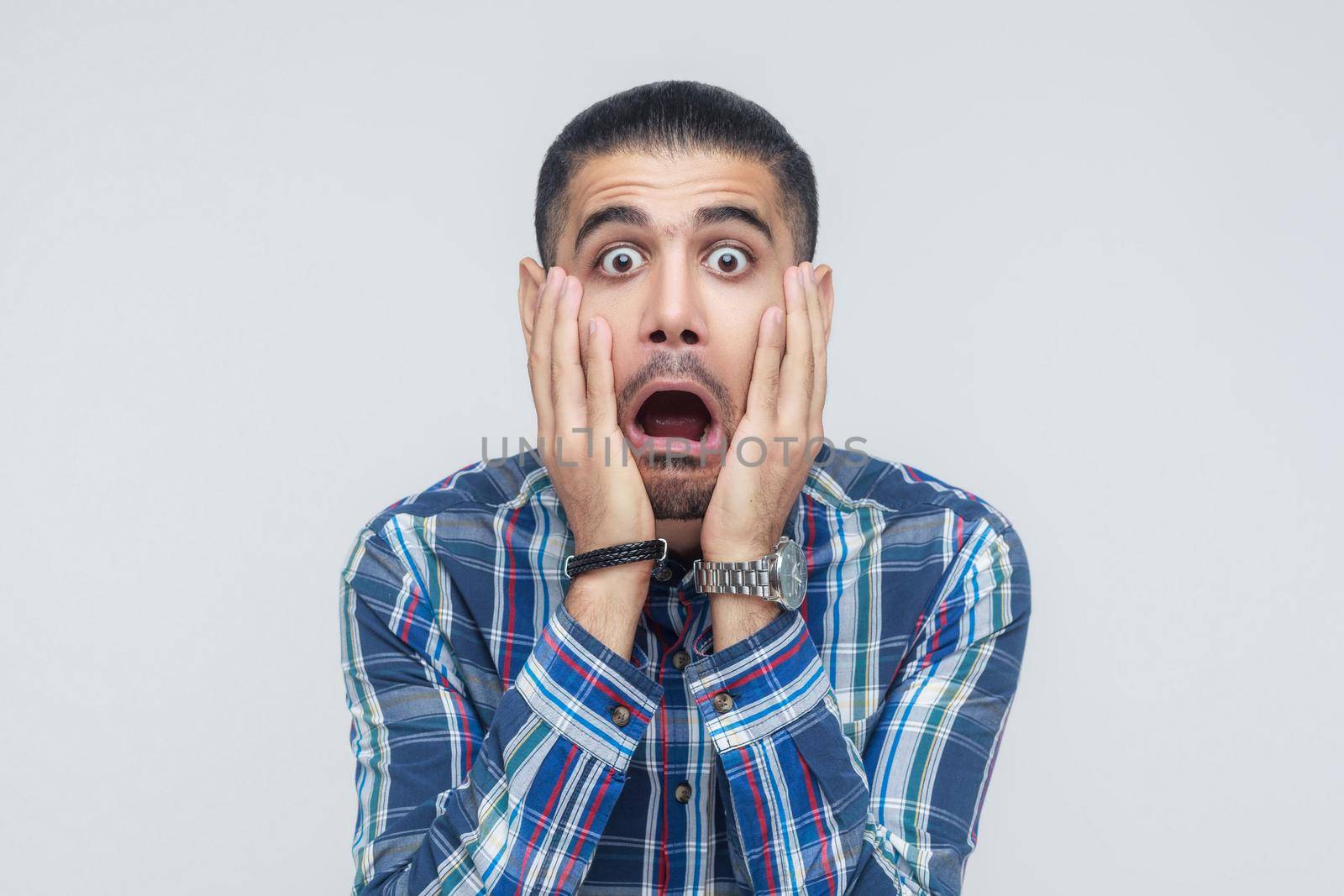 Human face expressions and emotions. Man holding arms on her cheeks, opened mouth and scream. Isolated studio shot on gray background.