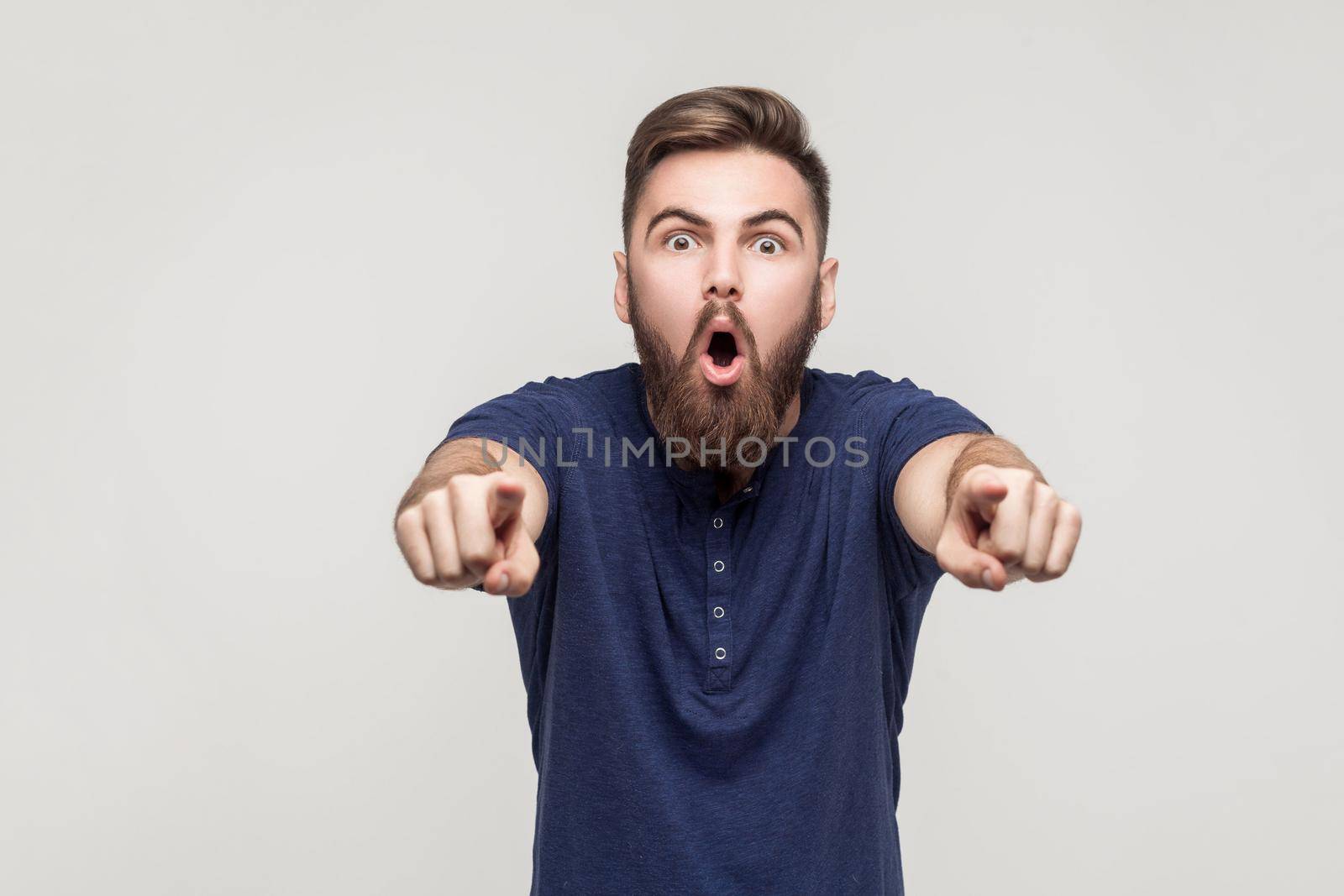 Hey you! Amazement bearded man pointing fingers at camera with open mouth and big eyes. Studio shot