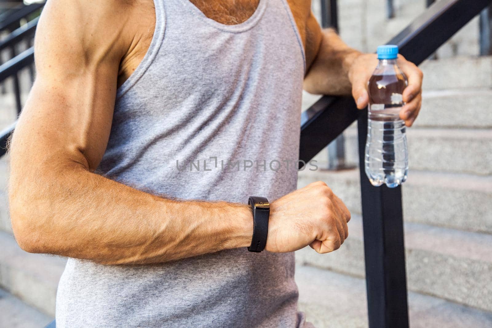 Sportsman with bottle of water is resting and checking his smart watch after running. fitness, sport, exercising and people healthy lifestyle concept.