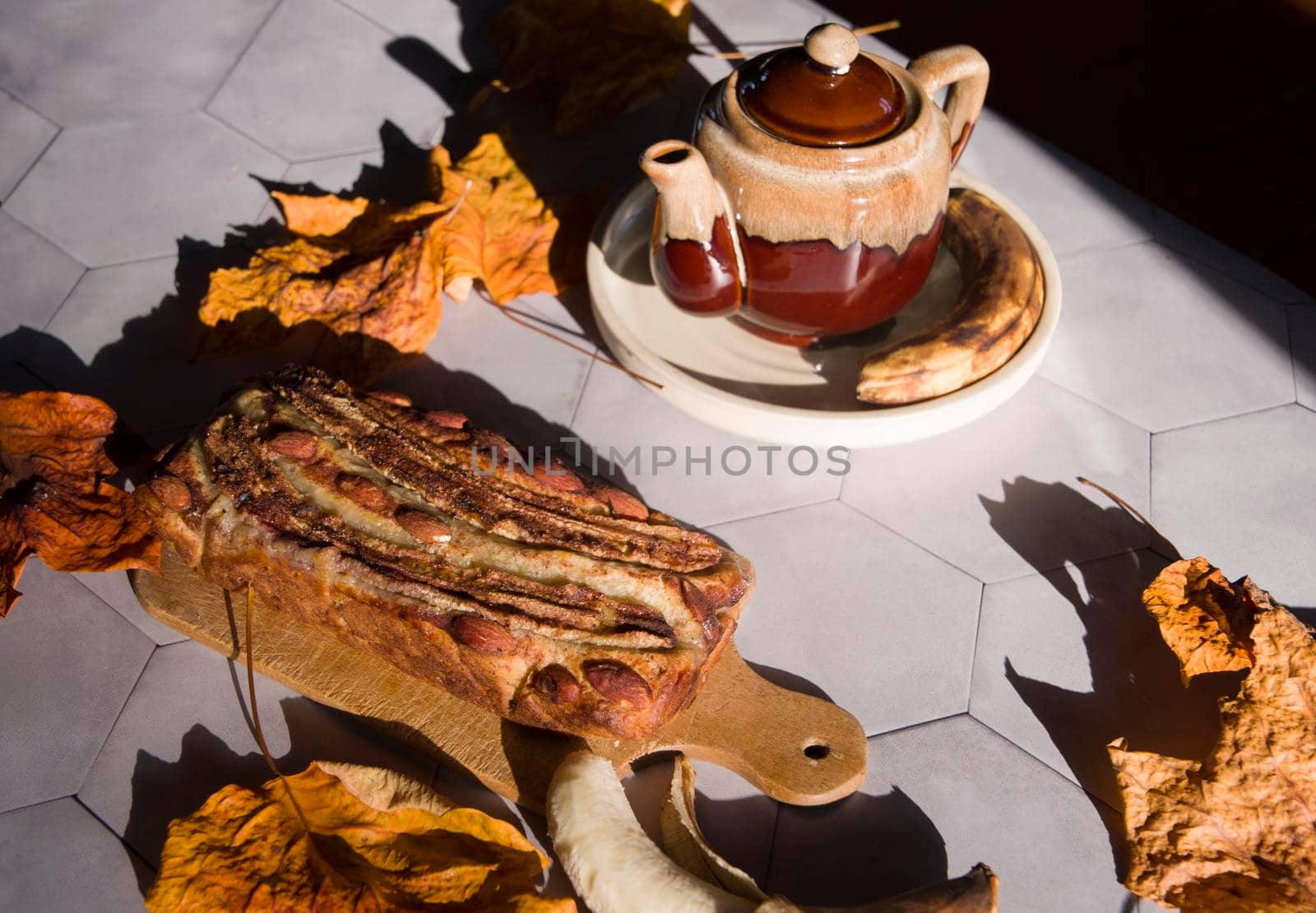 Still life Banana pie with a ceramic teapot in the rays of the autumn sun on a gray tile table. High quality photo