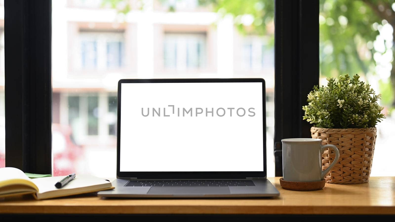 Front view laptop computer, coffee cup, houseplant and notebook on white table. Comfortable workplace by prathanchorruangsak