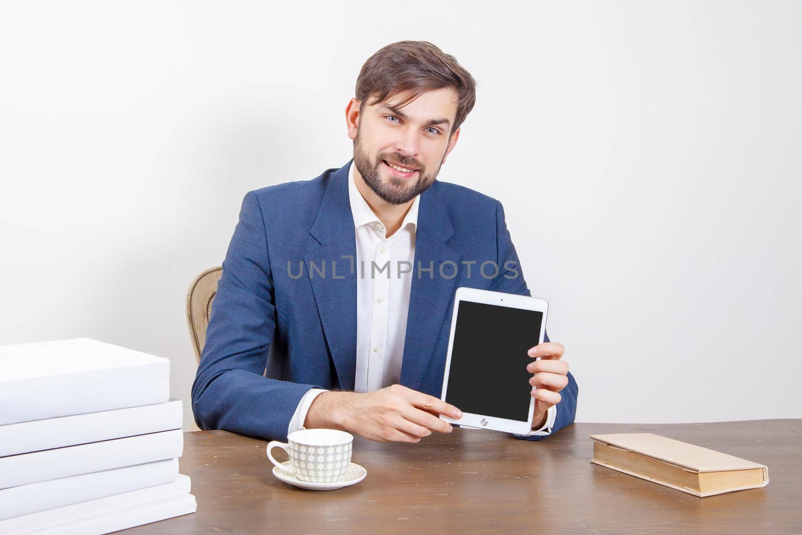 Technology, people and business concept - handsome man with beard and brown hair and blue suit and tablet pc computer and some books in the office holding tablet and showing display screen. .Isolated on white background. .