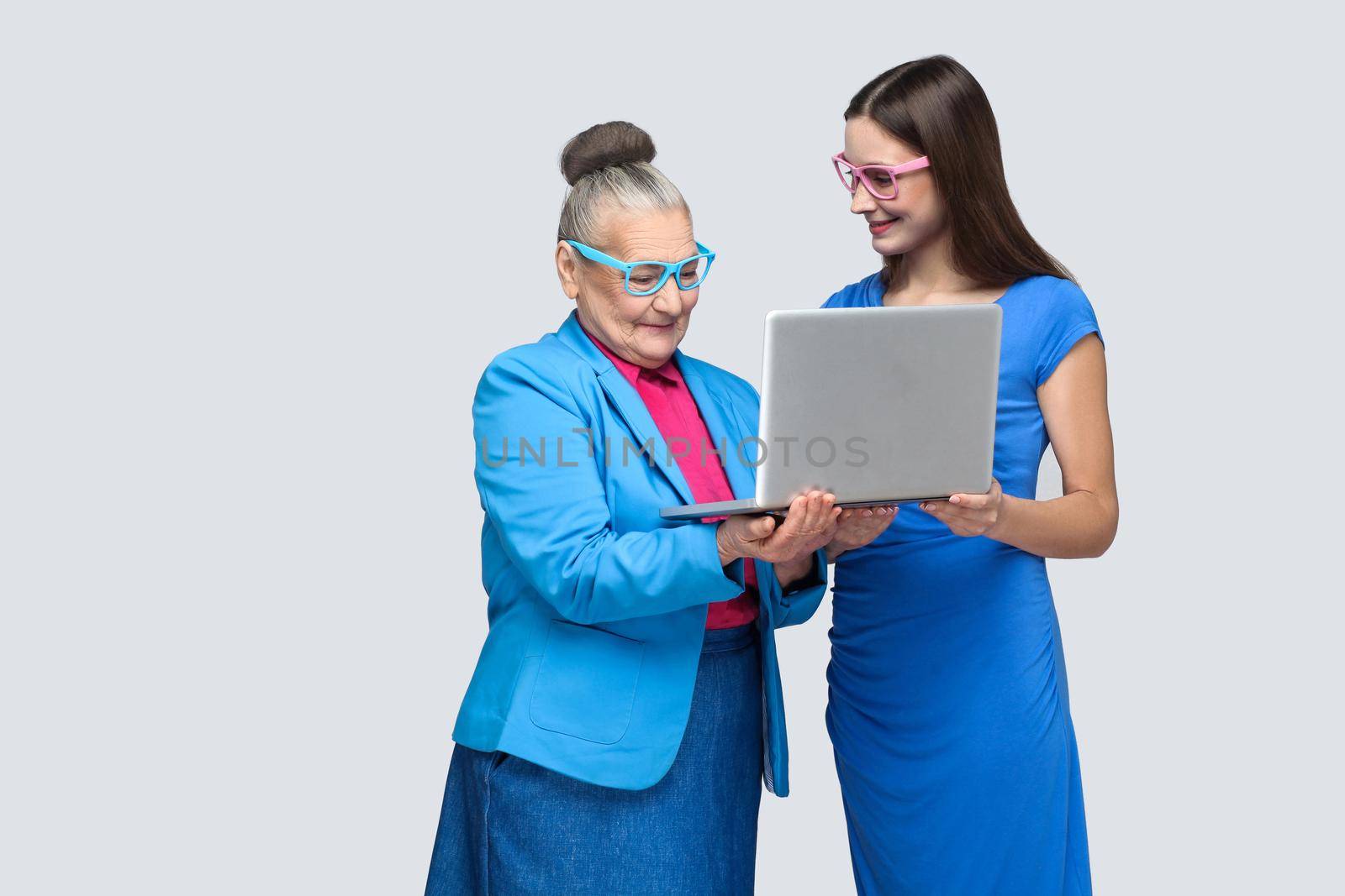 happy grandmother education or woman for work in social networking. granddaughter trying to teach her grandma to use laptop and working on internet. indoor, studio shot, isolated on gray background.