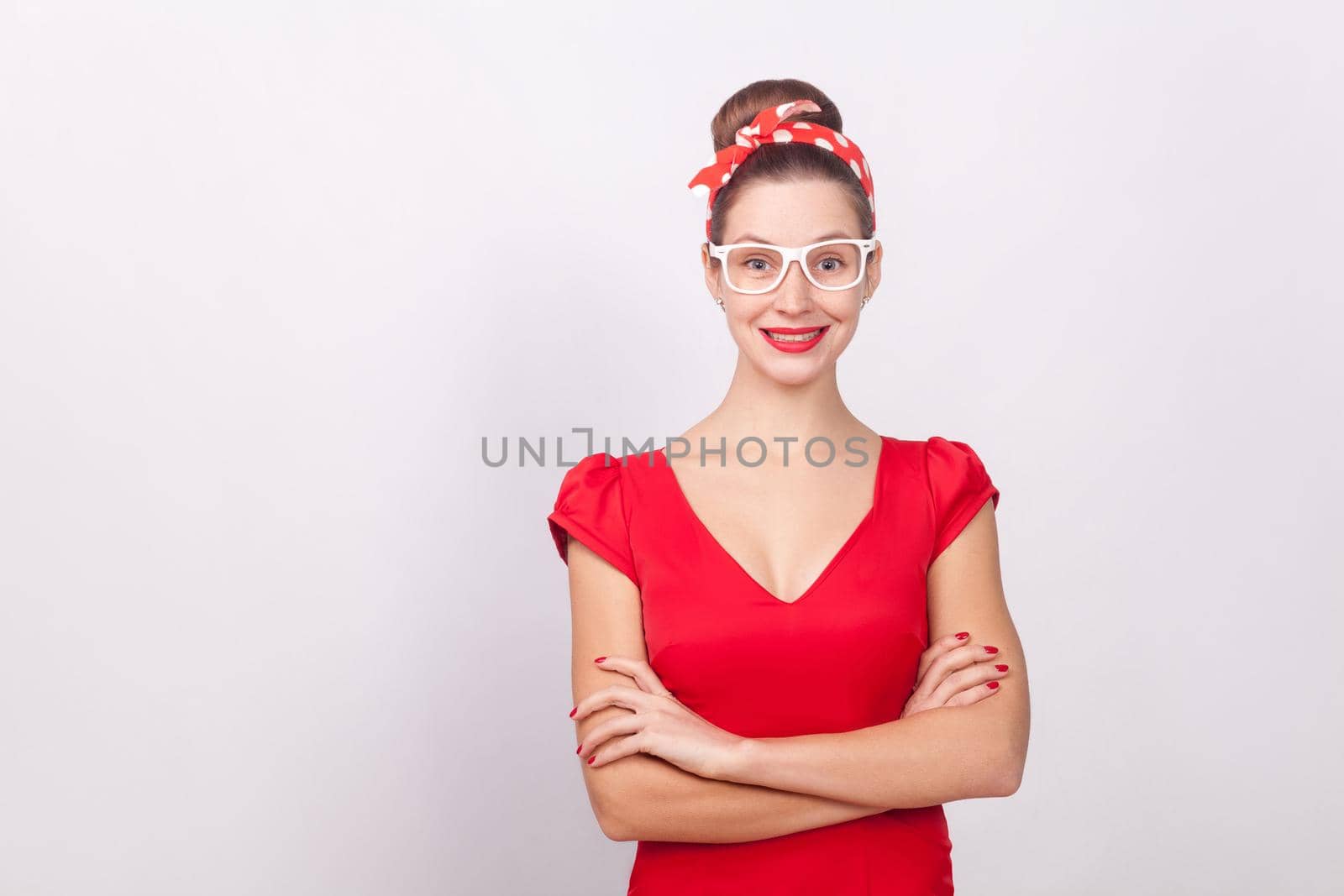 Cheerful beautiful woman in red dress and white glasses smiling. Indoor, studio shot, isolated on gray background