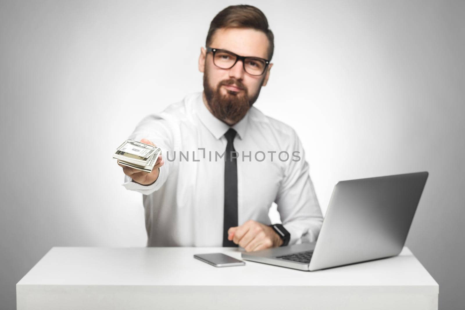 Money are yours! Portrait of handsome richman bearded young big boss in white shirt and black tie are sitting in office giving your a lot of money, your bonus, looking at camera, isolated, indoor