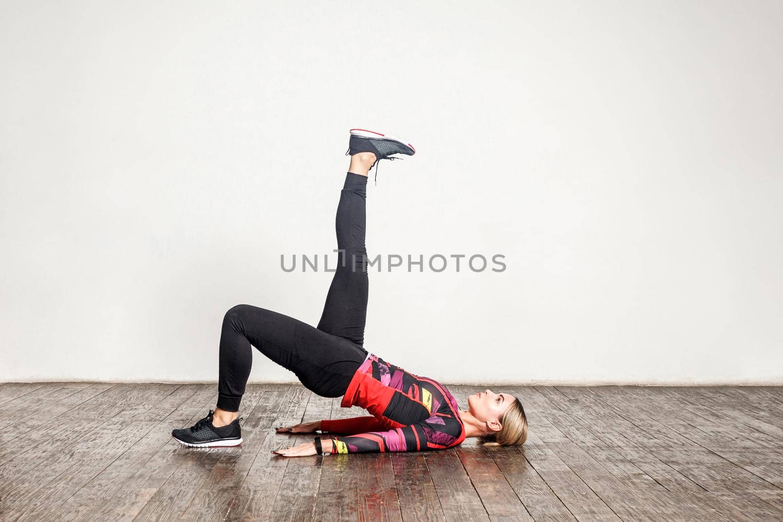 Young slim woman practicing yoga, doing one legged bridge pose with leg raise, training flexibility by Khosro1