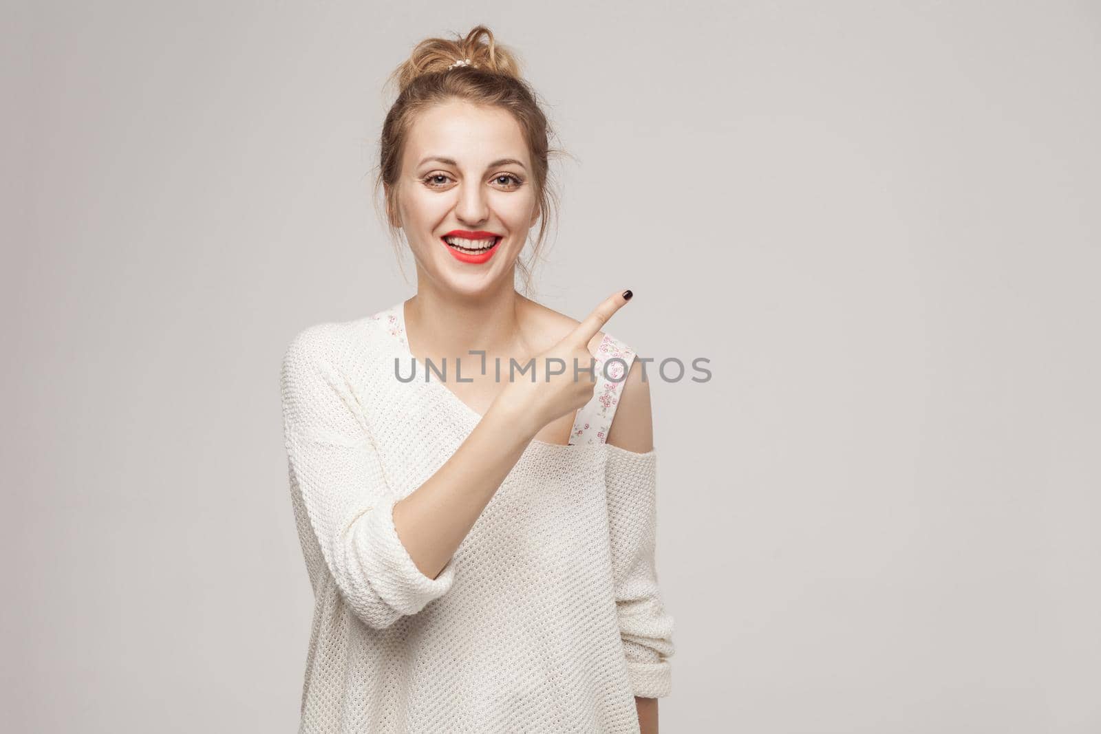 Successful blonde woman pointing finger at copy space and smiling.Studio shot, gray wall